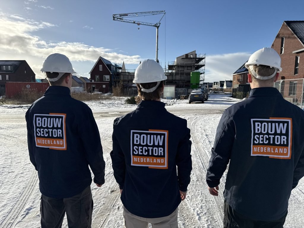 Drie medewerkers van Bouwsector Nederland met witte helm voor een rij nieuwe woningen in aanbouw
